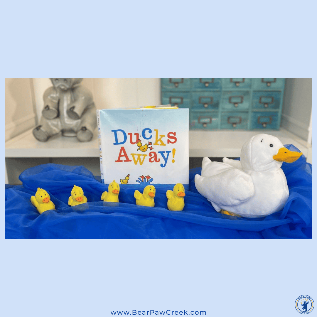 Blue canopy scarf with five small plush ducks and one large plush duck next to a book.